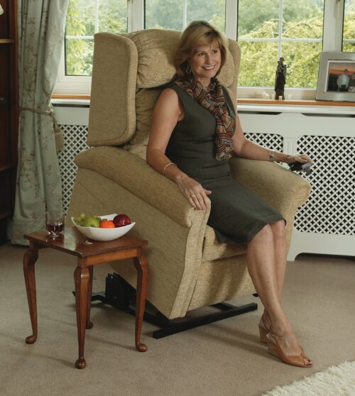 Woman sitting on a beige riser recliner chair in a living room.