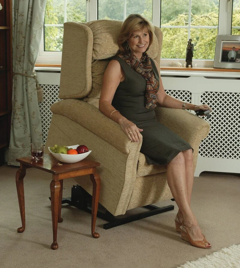 Woman sitting on a beige riser recliner chair in a living room.