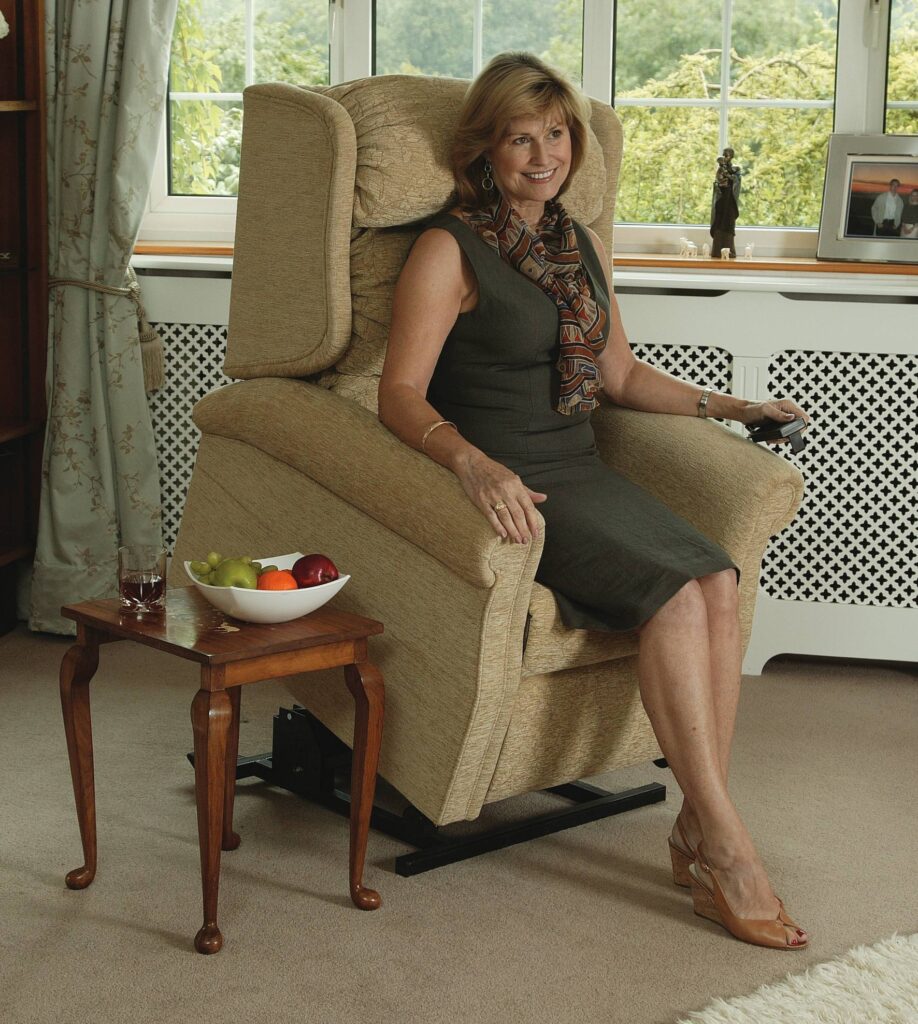 Woman sitting on a beige riser recliner chair in a living room.