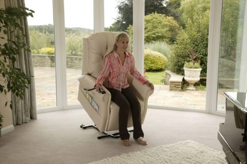 Woman sitting on a recliner in a bright room with large windows.