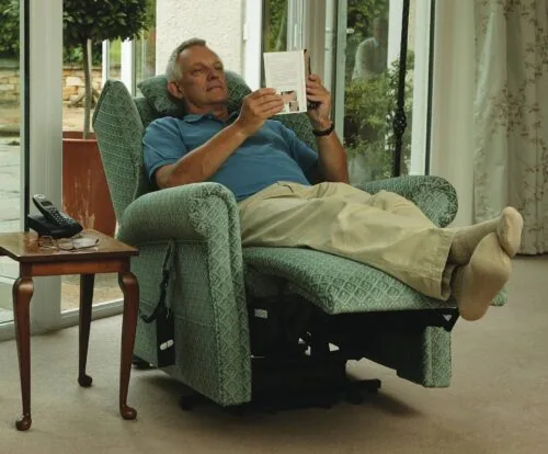 Man reading in a green recliner chair next to a small table with a phone.