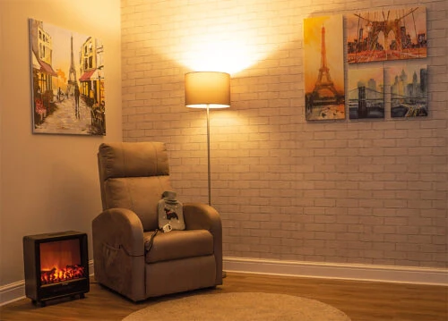 Electric recliner chair in a cozy living room setup with art and a lamp.