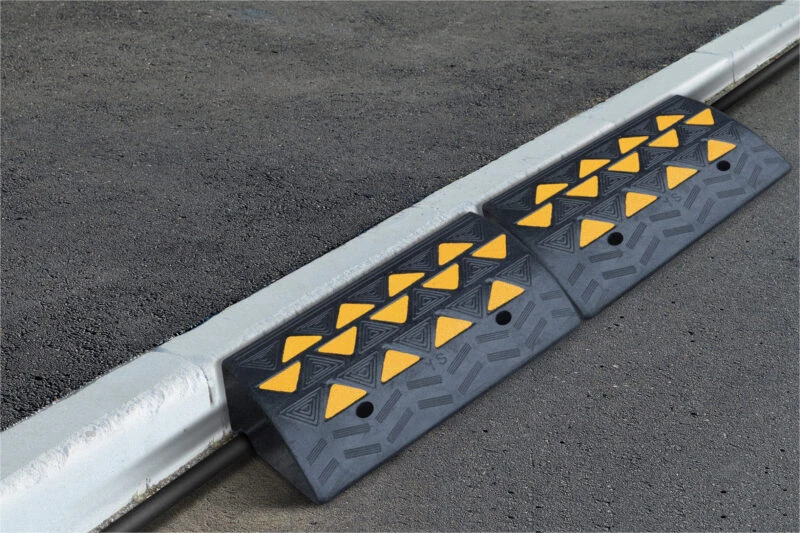 Rubber kerb ramp with yellow reflective panels on a concrete kerb.