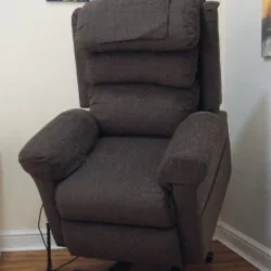 Brown riser recliner armchair positioned in a corner of a room.