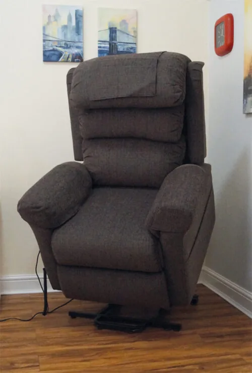 Brown riser recliner armchair positioned in a corner of a room.