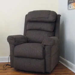 Brown riser recliner armchair in a corner with wall art.