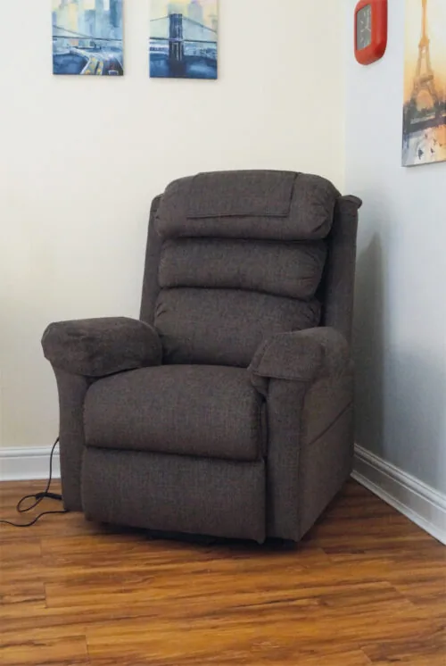 Brown riser recliner armchair in a corner with wall art.