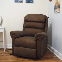 Brown riser recliner armchair in a room with wall art and a side table.