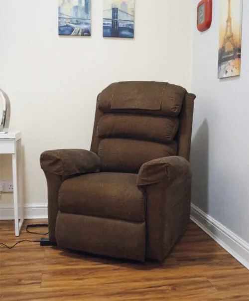 Brown riser recliner armchair in a room with wall art and a side table.