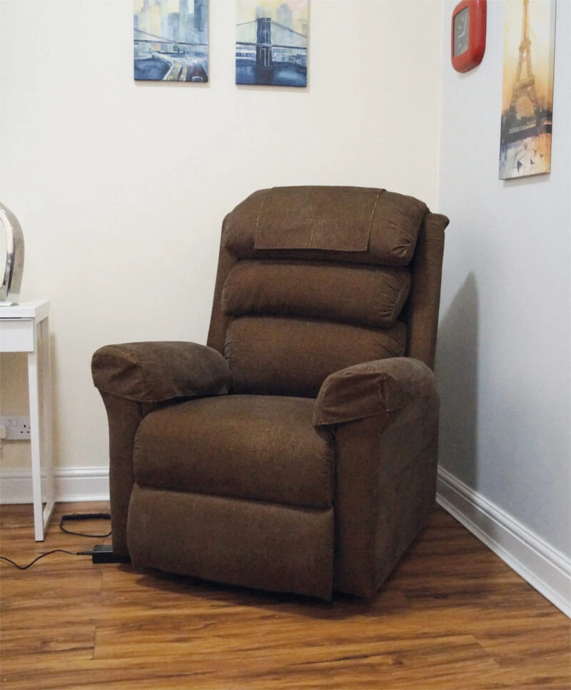 Brown riser recliner armchair in a room with wall art and a side table.