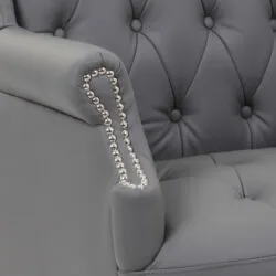 Close-up of a grey armchair with tufted back and nailhead trim.