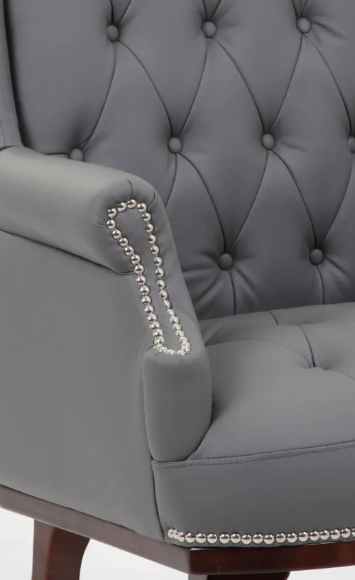 Close-up of a grey armchair with tufted back and nailhead trim.