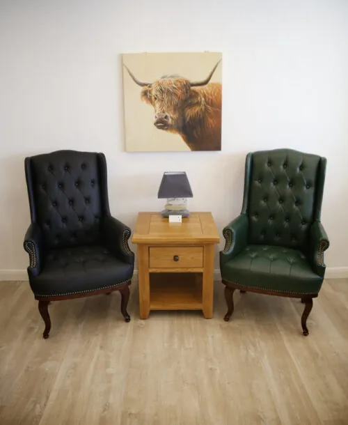 Two high back armchairs, one black and one green, flanking a wooden side table.