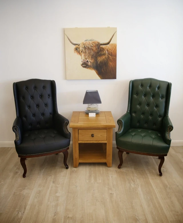 Two high back armchairs, one black and one green, flanking a wooden side table.