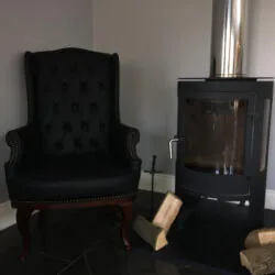 Black high back armchair next to a modern fireplace with logs.