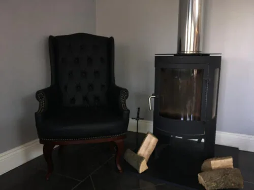Black high back armchair next to a modern fireplace with logs.