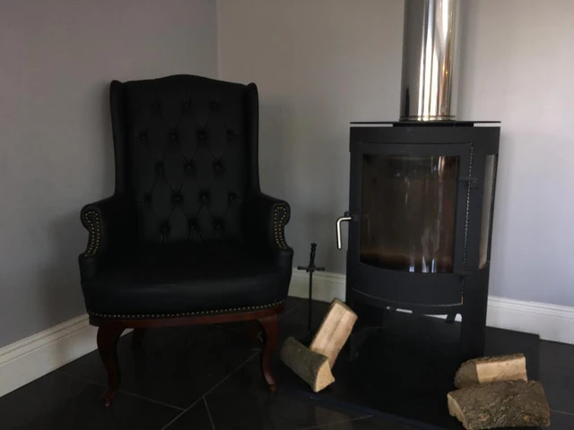 Black high back armchair next to a modern fireplace with logs.
