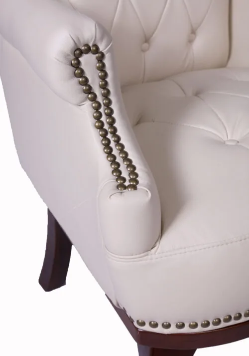 Close-up of cream armchair with studded armrest and dark wooden legs.