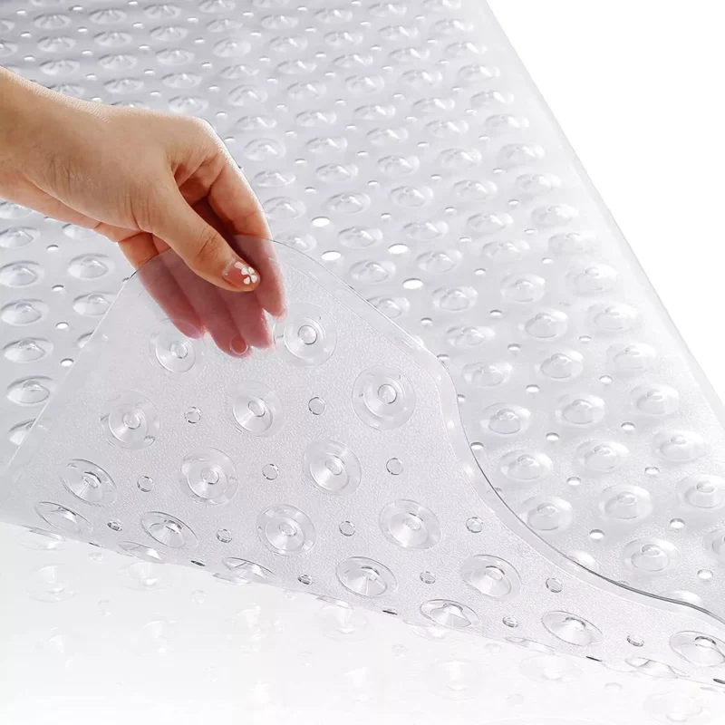 Hand lifting corner of clear anti slip shower mat with suction cups.