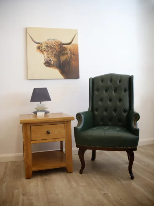 Green high back armchair next to a wooden side table with a lamp.