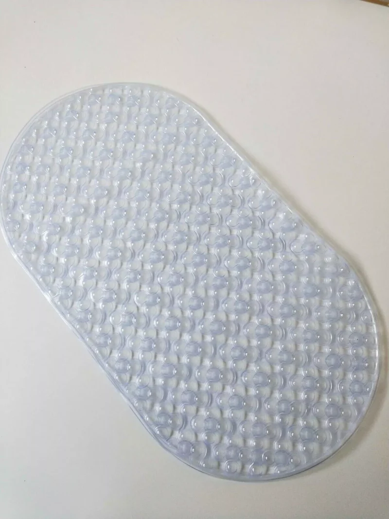 Clear oval shower mat with suction cups on a white surface.