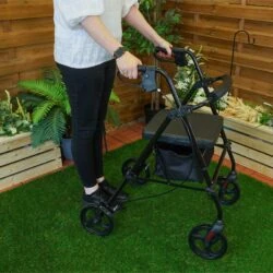Person using a black rollator with seat and under-seat storage on grass.