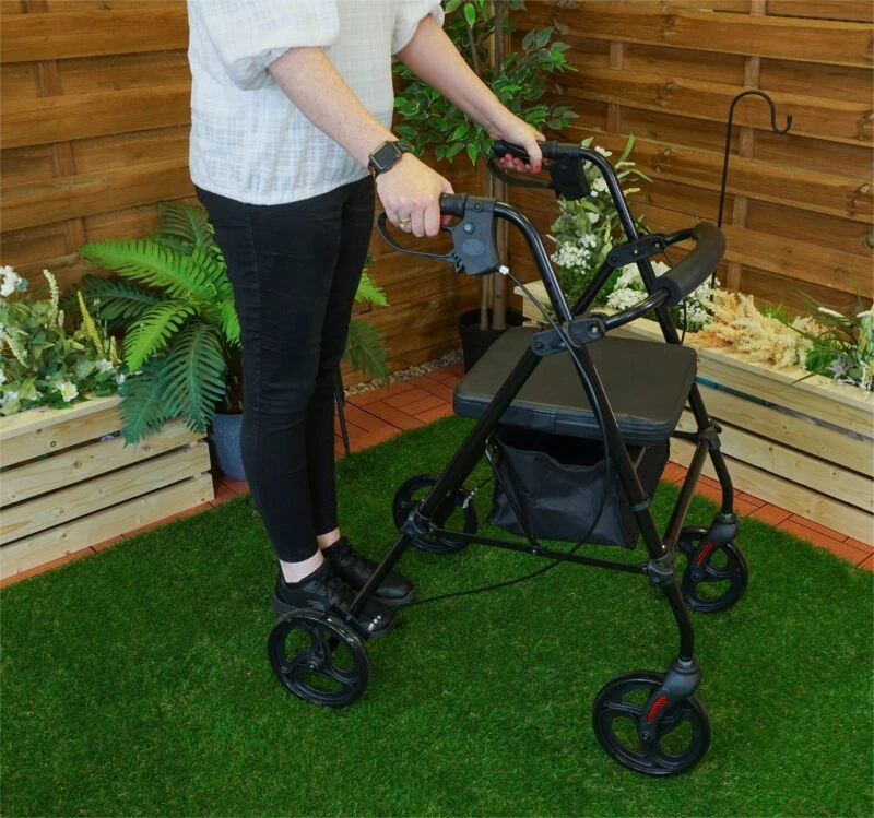 Person using a black rollator with seat and under-seat storage on grass.
