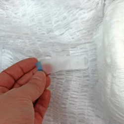 Close-up of a hand holding a tab on a textured white pull-up pant.