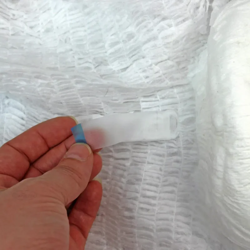 Close-up of a hand holding a tab on a textured white pull-up pant.