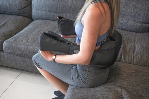 Person sitting on a couch using a neck and shoulder massager.