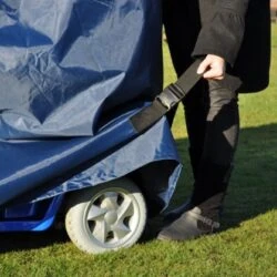 Person securing a navy waterproof cover over a mobility scooter on grass.