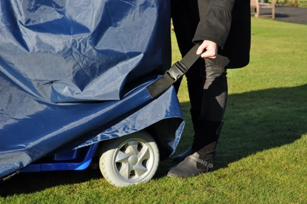Person securing a navy waterproof cover over a mobility scooter on grass.