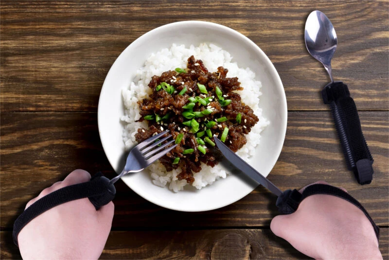 Person using adaptive silverware with straps to eat rice and meat.