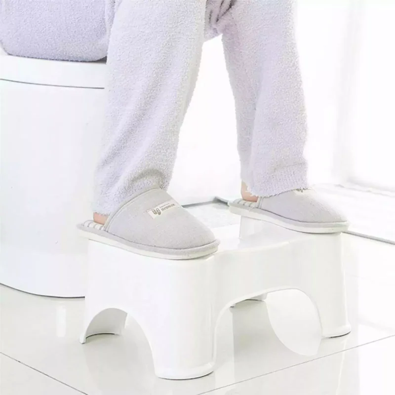 Person using a white toilet foot stool while seated on a toilet.