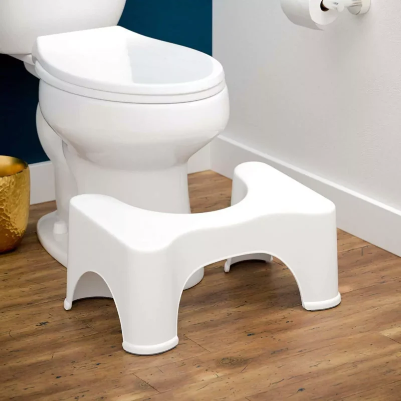 White toilet foot stool placed in front of a toilet.