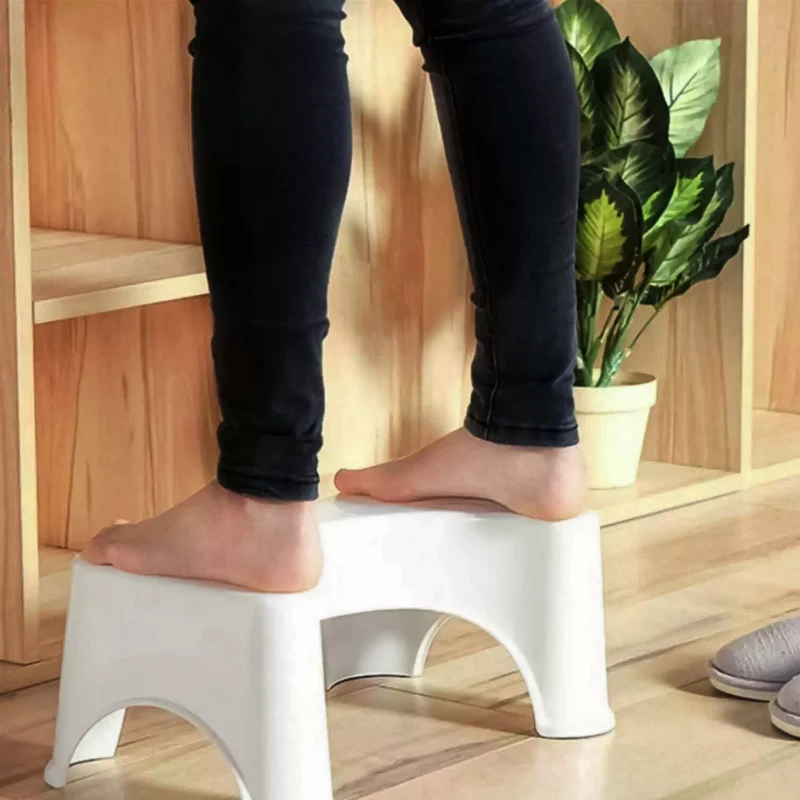 Person standing barefoot on a white toilet foot stool indoors.