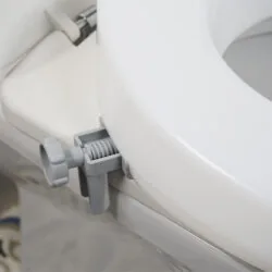 Close-up of a toilet seat extender with a grey bracket attached.