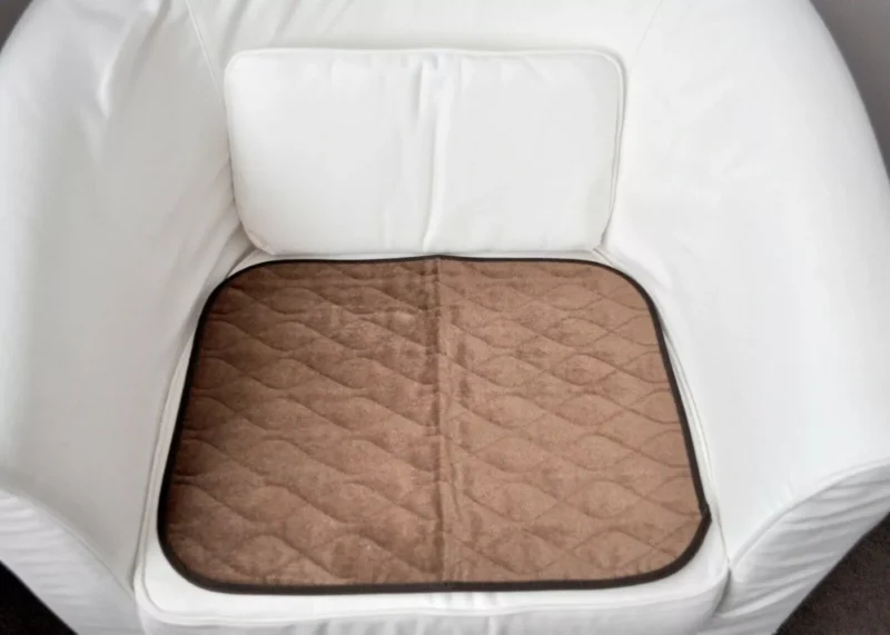 Brown incontinence chair pad placed on a white chair.