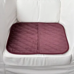 Burgundy incontinence chair pad placed on a white armchair.