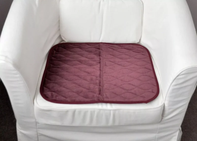 Burgundy incontinence chair pad placed on a white armchair.