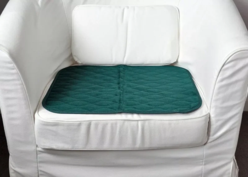Green incontinence chair pad placed on a white chair.