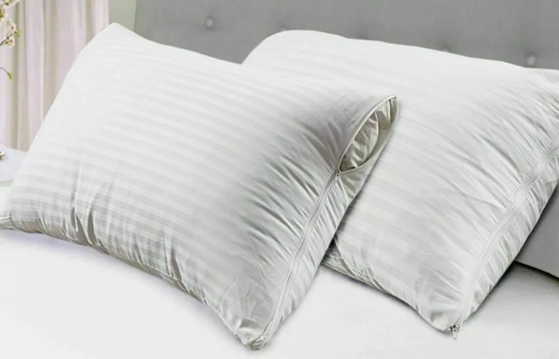 Two white striped pillow covers with zippers on a bed.