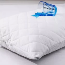 A glass of blue liquid spilled on a quilted white pillow protector.