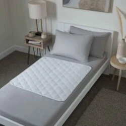 Bed with a quilted white bed protector on gray sheets.