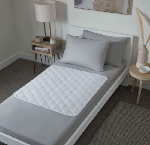 Bed with a quilted white bed protector on gray sheets.