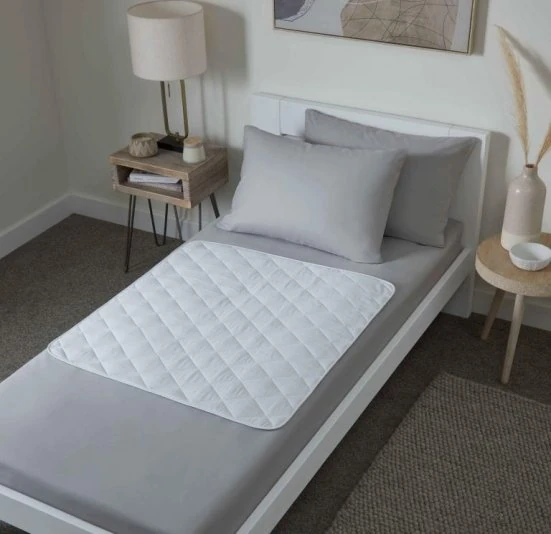 Bed with a quilted white bed protector on gray sheets.