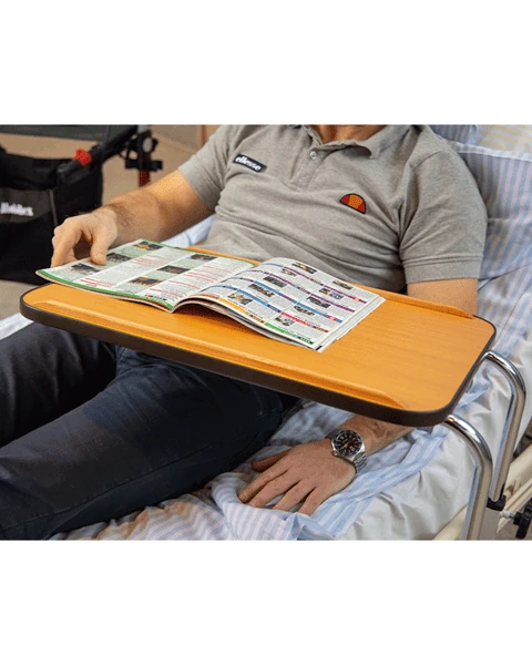 Person using a hospital overbed table while reading a magazine.