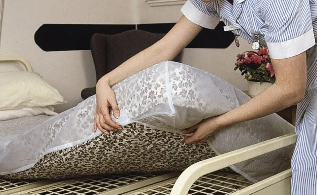 Nurse fitting a waterproof mattress protector on a bed.