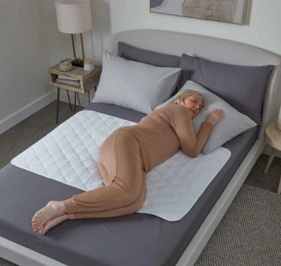 Person lying on a bed with a quilted bed protector.