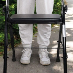 Person using a foldable walker with a padded seat outdoors.
